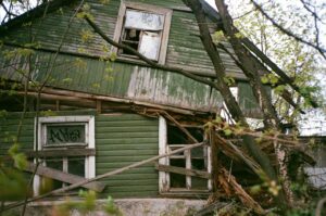 Exterior of an older home with peeling paint and overgrown yard — example of a distressed house ready to sell.